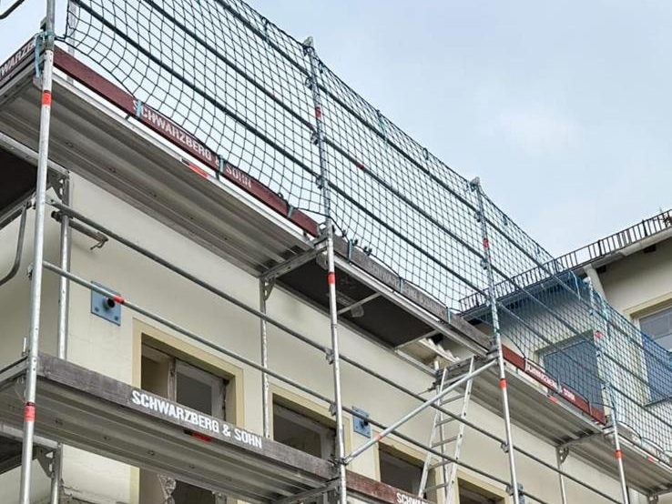 Fassadengerüst mit Schutznetz und Firmenbanner an einem Wohnblock