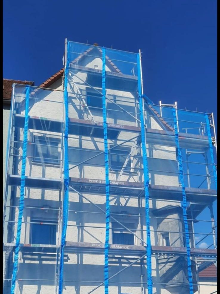 Mehrgeschossiges Fassadengerüst mit blauem Schutznetz an einem Wohnhaus
